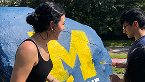 Two students painting the rock with a michigan M