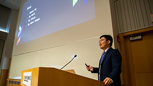 Xucong Zhen presenting at a podium with a presentation in the background