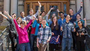 Group photo of Dr. Michaela Zint and her students posing with their hands in the air in front of an academic building