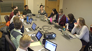 Students seated around a large table with laptops in discussion