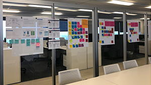 Large easel pages covered in multi-colored sticky notes adhered to glass walls in the Office of Academic Innovation