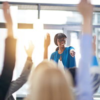 Woman pointing to a crowd of business professionals raising their hands