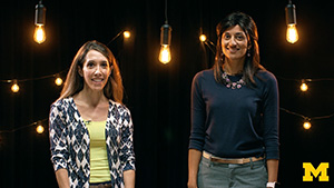 Dr. Cathy Goldstein and Dr. Anita Valanju Shelgikar standing in a filming studio smiling at the camera, surrounded by light bulbs