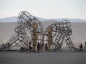 Large wire sculpture of two adults sitting facing away from each other with solid structures of children inside the wire frames reaching out to each other