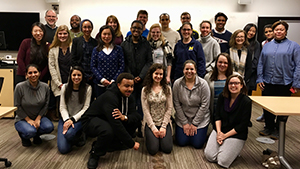 A diverse group of students standing in a classroom and smiling at the camera.