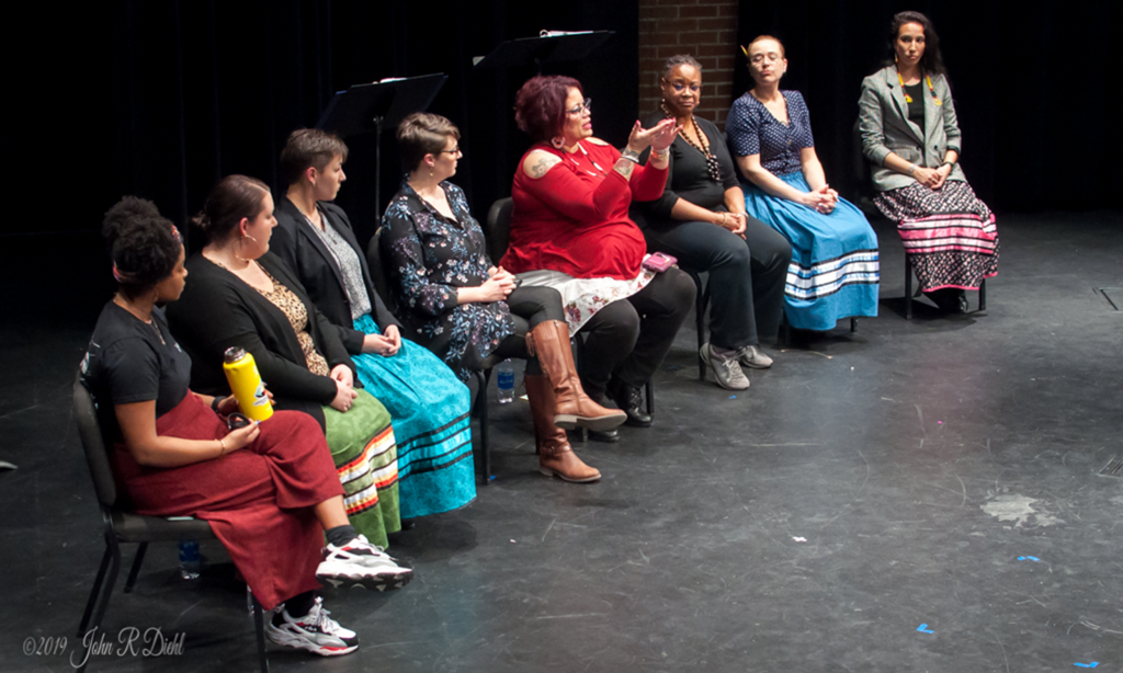 Actors in a class seated on stage in a line