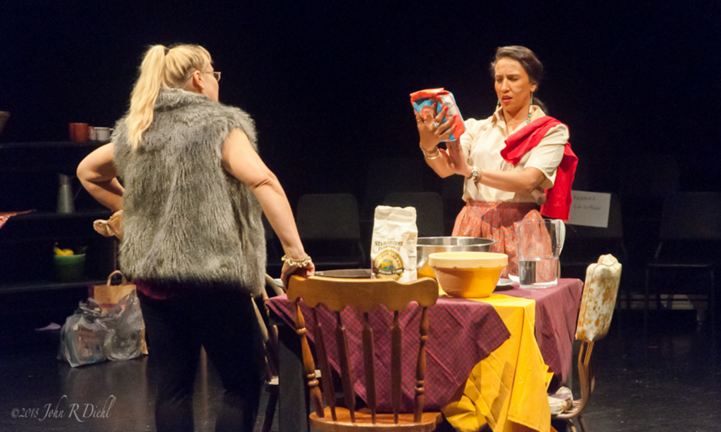 Two female actors acting out a scene with a table in between them