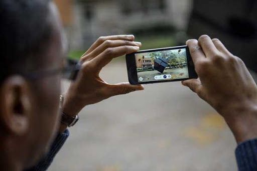 Man holding up smart phone with extended reality elements on screen on U-M's campus