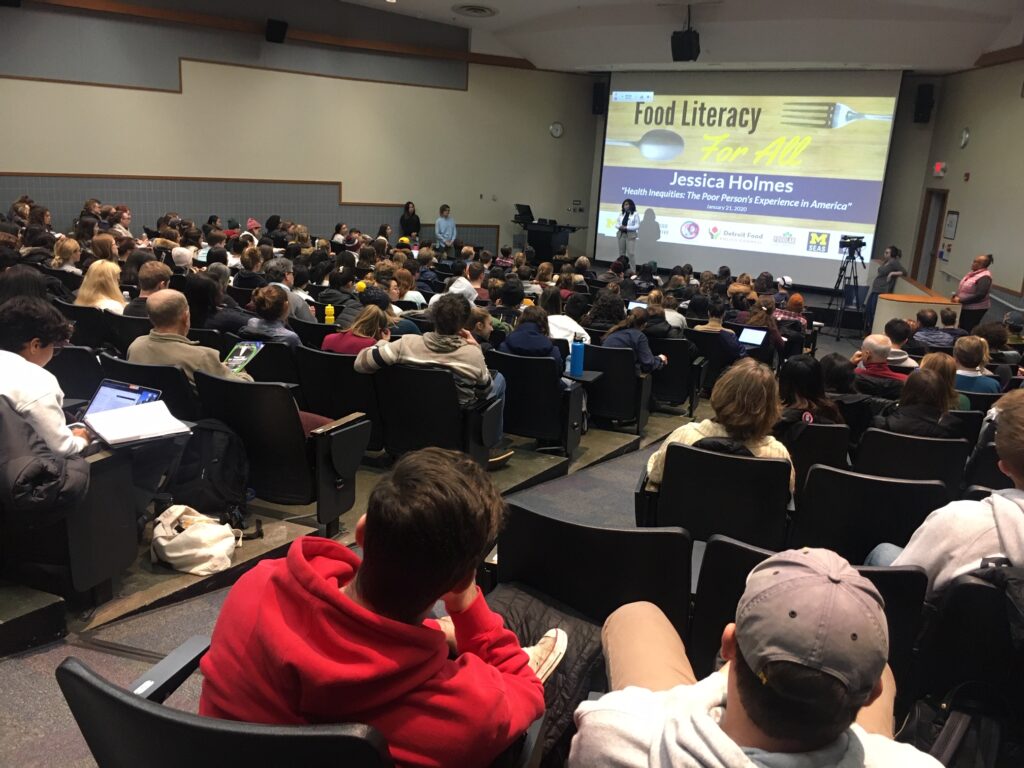 lecture hall full of people looking at speaker giving presentation.