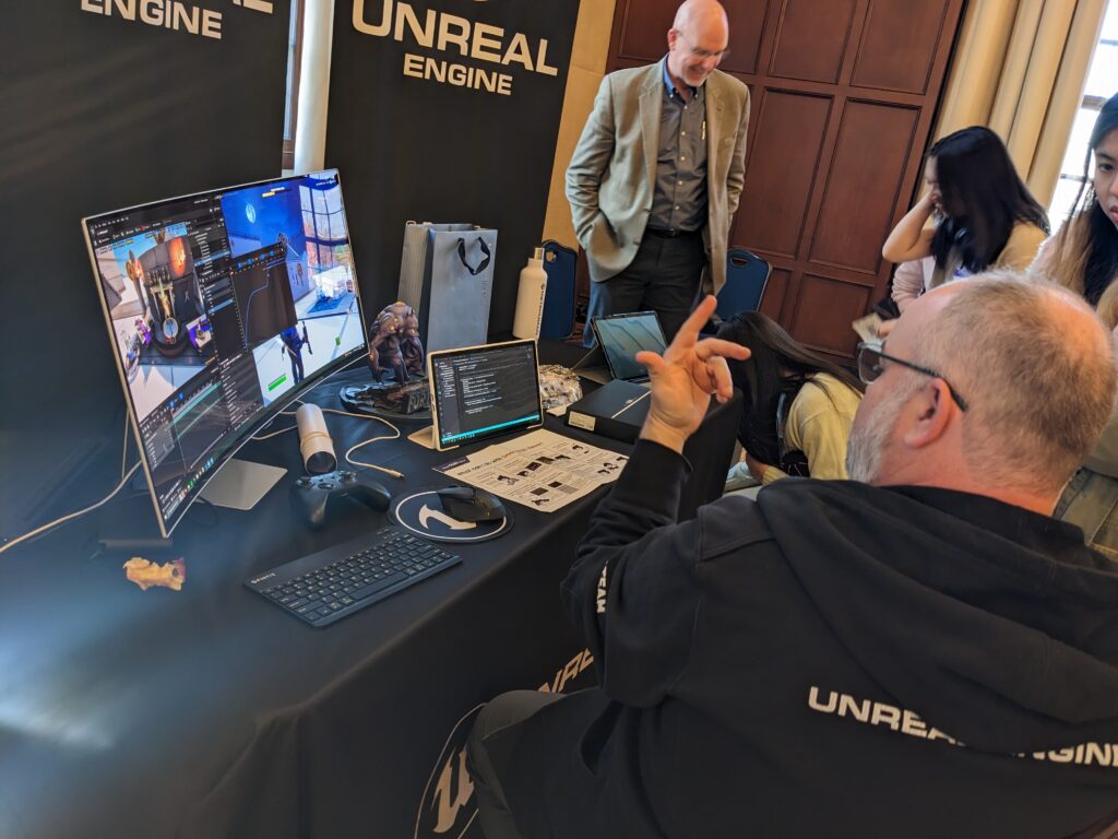 man in front of computer monitors talking to attendees 