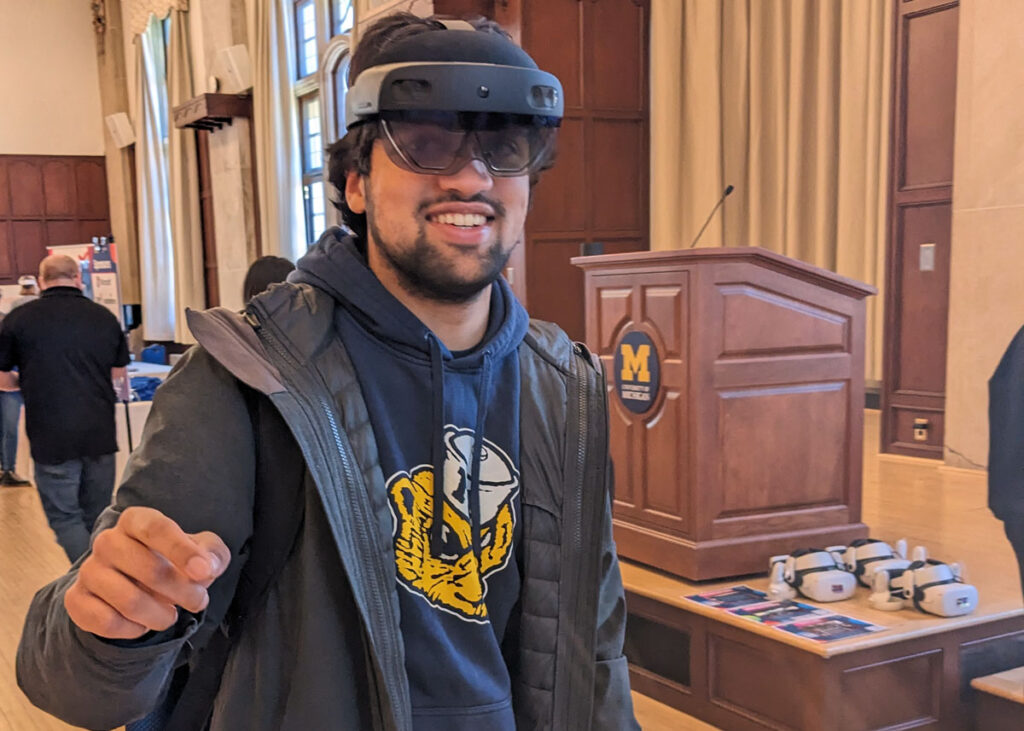 Man with Hololens headset gestures his hand forward while looking at the camera.