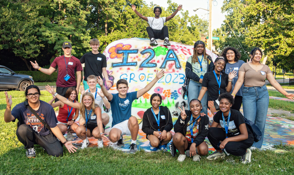 group of students gather around the painted rock that says I2A GROE 2023