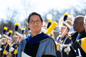 Santa Ono in cap and gown at ceremony with band members in background