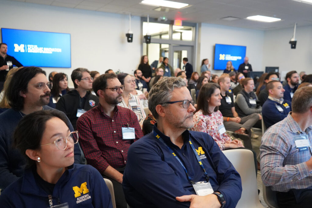 Man sits with arms folded among a crowd sitting and listening to a presenter.