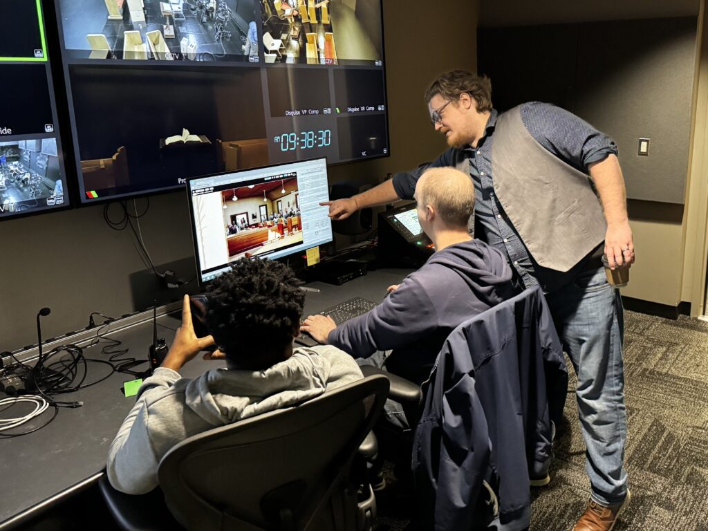 A many points at a computer screen with two others close by. 