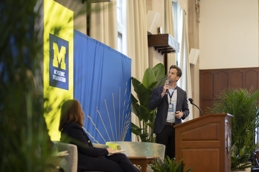 Man speaking at a lecturn looks up at a screen behind him