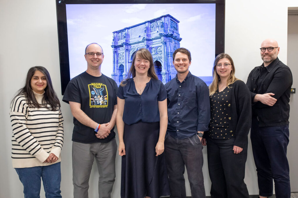 Five people stand together in front of a large screen displaying the Arch of Constantine.
