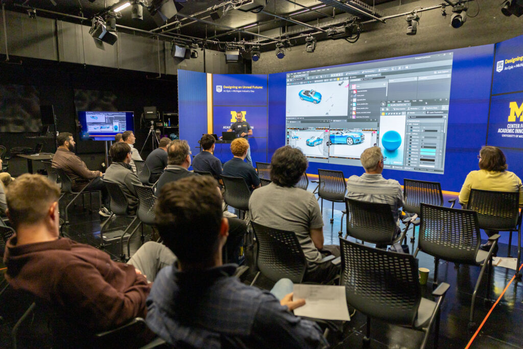 An audience watches a live Unreal Engine demonstration on a large screen during an Epic Games event at the University of Michigan Center for Academic Innovation.
